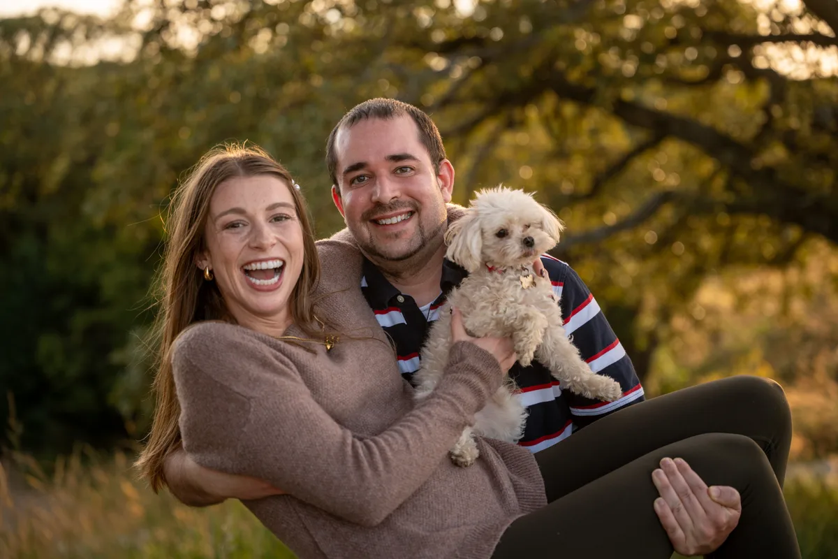 A newly engaged couple laughing together with their small white dog just after the proposal, Mahoney State Park, Nebraska