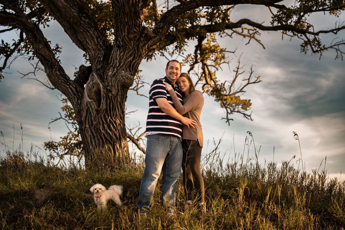 Newly engaged couple and their dog under a large oak at sunset, Mahoney State Park, Nebraska